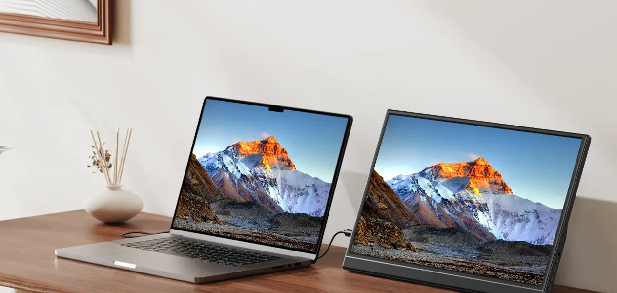 A laptop and a YXK portable monitor side by side on a wooden desk, both showing the same mountain view